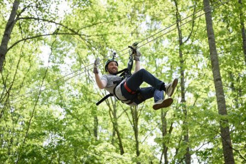A person zip-lining through a lush green forest, smiling and enjoying the adventure.