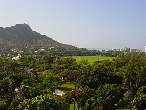 A scenic view of lush greenery, mountains, and a distant ocean under a clear blue sky.