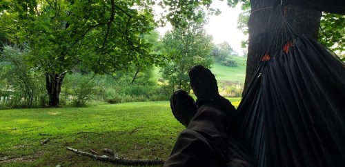 A person relaxing in a hammock under trees, with feet visible and a serene landscape in the background.