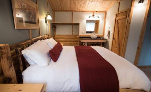 Cozy bedroom with a wooden bed, white linens, and a red throw, featuring rustic decor and warm lighting.
