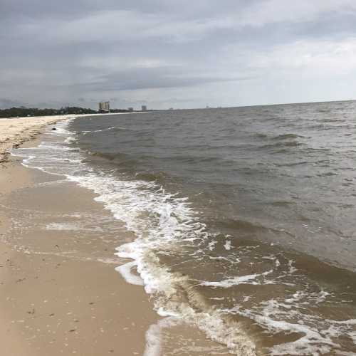 A sandy beach with gentle waves lapping at the shore, under a cloudy sky.