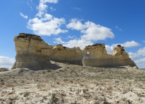 Rock formations against a blue sky with clouds, surrounded by dry terrain.