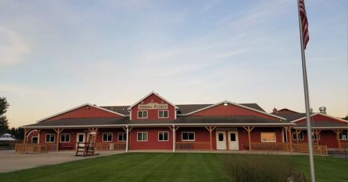 A red barn-style building with a grassy area in front, featuring a flagpole and a clear blue sky.