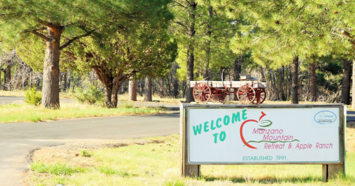 Sign welcoming visitors to Manzano Mountain Retreat & Apple Ranch, with a vintage wagon and trees in the background.