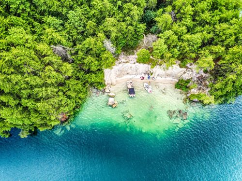 Aerial view of a serene beach surrounded by lush greenery and clear blue water, with boats anchored nearby.