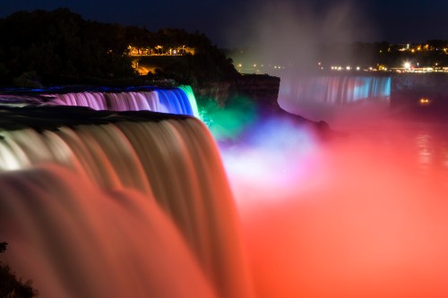 Niagara Falls illuminated at night with colorful lights, creating a vibrant mist and serene atmosphere.