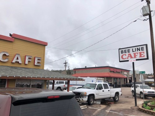 A cloudy day view of Bee Line Cafe and nearby buildings, with parked white trucks in the foreground.