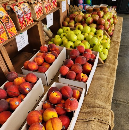 Baskets of fresh peaches and green apples displayed on a wooden table at a market.
