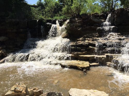 A serene waterfall cascading over rocky terrain into a calm pool, surrounded by lush greenery.