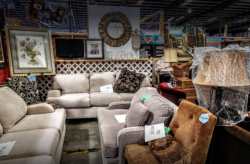 A variety of used furniture, including sofas, chairs, and decor, displayed in a warehouse setting.
