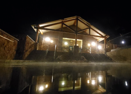 A serene building at night, illuminated with warm lights, reflecting in a calm water pool.