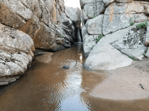 A narrow stream flows between large rocky formations, with a small waterfall visible in the background.