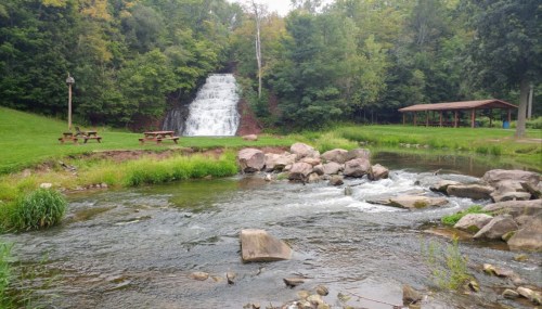 A serene landscape featuring a waterfall, flowing river, and picnic area surrounded by lush greenery.