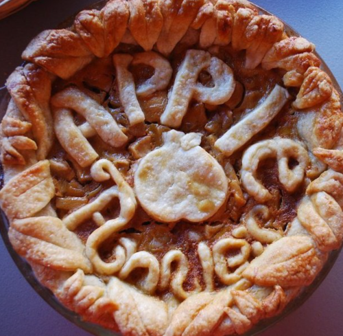 A freshly baked apple pie with a decorative crust spelling "Happy" and "Fall" on top.