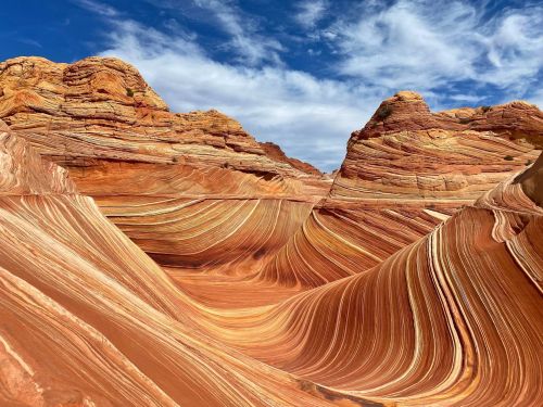 Colorful, undulating rock formations with layered stripes under a blue sky, showcasing natural erosion patterns.