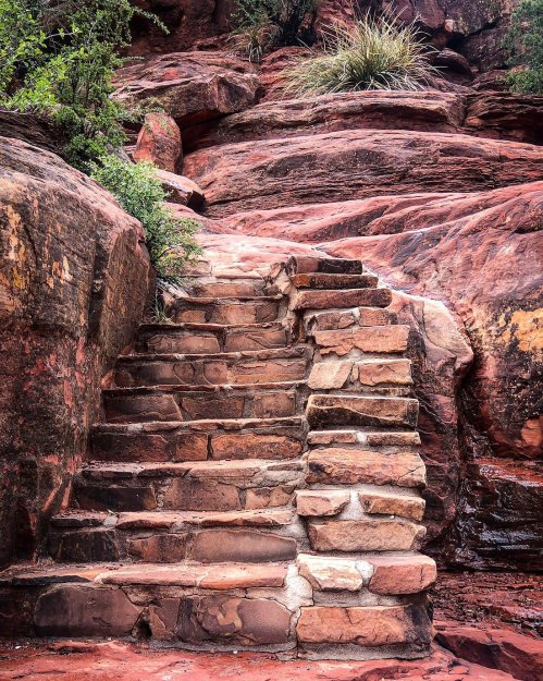 Stone steps carved into a red rock landscape, surrounded by greenery and rugged terrain.