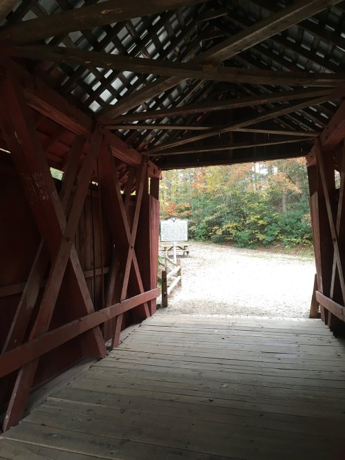 View from inside a covered bridge, showcasing wooden beams and a glimpse of nature outside.