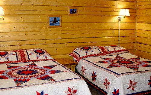 Cozy wooden room with two beds featuring star-patterned quilts and warm lighting.
