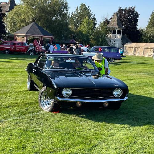 A classic black car parked on green grass, with people admiring it in a car show setting.