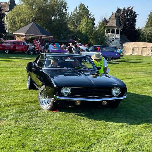 A classic black car parked on green grass, with people admiring it in a car show setting.