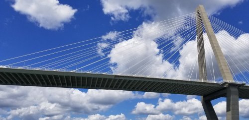 A suspension bridge with a tall tower and cables against a blue sky filled with fluffy white clouds.