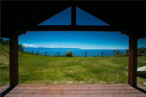 View from a wooden gazebo overlooking a lush green lawn and a serene blue ocean with distant mountains.