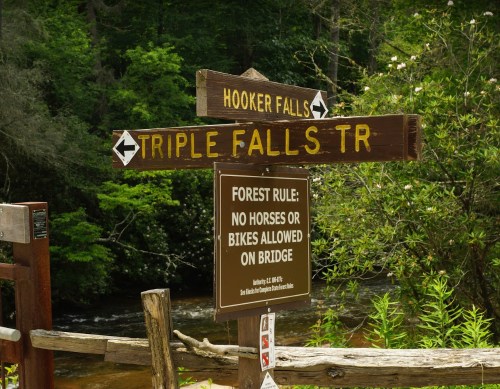 Wooden signpost indicating directions to Hooker Falls and Triple Falls Trail, with a rule about no horses or bikes on the bridge.