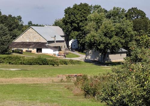 A scenic view of a farm with a large barn, surrounded by trees and open fields under a clear sky.