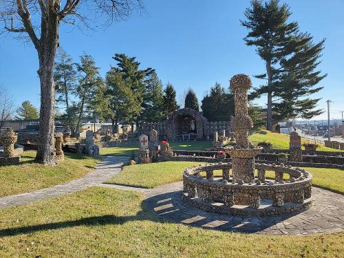 A stone fountain surrounded by landscaped gardens and trees under a clear blue sky.