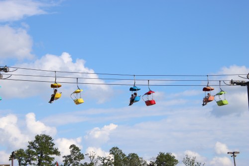 Colorful gondolas on a cable car ride against a blue sky with fluffy clouds and trees below.
