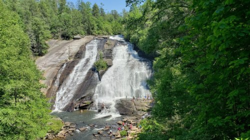 A scenic waterfall cascades down rocky cliffs, surrounded by lush greenery and visitors enjoying the water below.