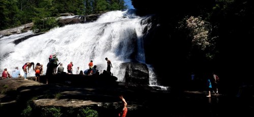 A waterfall cascades over rocks, with people enjoying the water and surrounding nature.