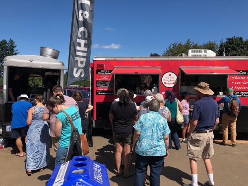 A crowd lines up at two food trucks on a sunny day, with a banner for fish and chips visible.