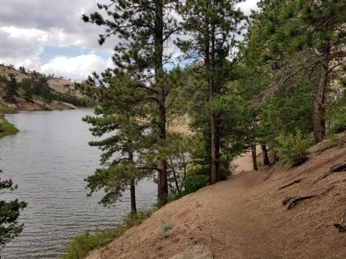 A serene lakeside scene with trees lining the shore and a sandy path leading along the water's edge.