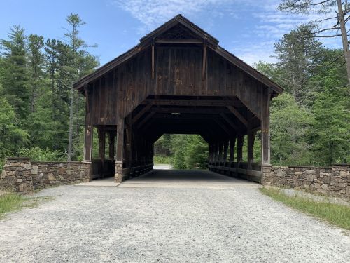 A wooden covered bridge with a stone foundation, surrounded by trees and a gravel path.