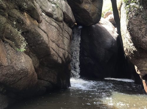 A waterfall cascades between large, moss-covered rocks in a serene natural setting.