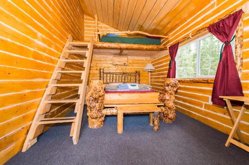 Cozy cabin interior with wooden walls, a lofted bed, and rustic furniture, featuring a staircase and a window with curtains.