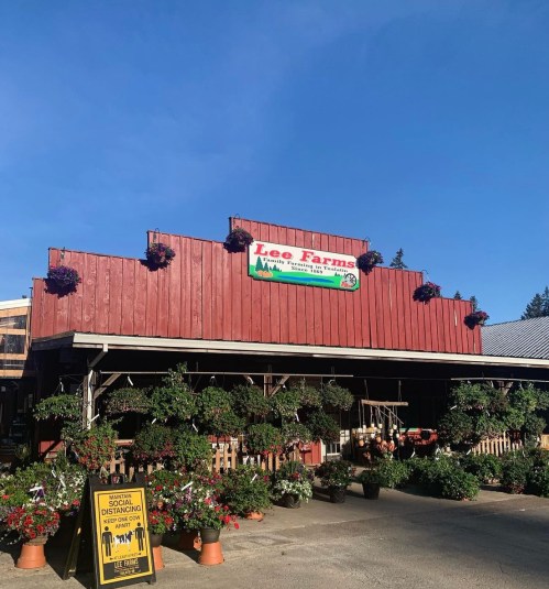 A red barn-style building with hanging flower baskets and a sign for Lee Farms under a clear blue sky.
