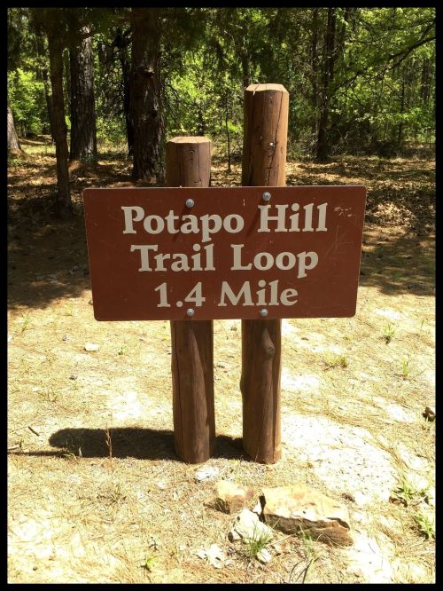 Sign for Potapo Hill Trail Loop, indicating a distance of 1.4 miles, surrounded by trees and natural scenery.