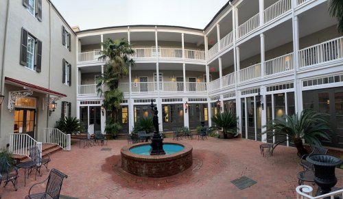 A courtyard with a fountain, surrounded by balconies and palm trees, featuring brick pathways and seating areas.