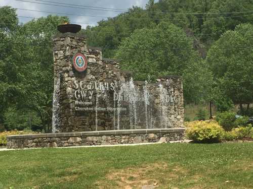 Stone welcome sign with a fountain, surrounded by greenery, featuring the Cherokee Nation logo.