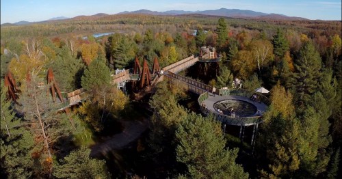 Aerial view of a scenic outdoor park with wooden walkways, surrounded by colorful autumn trees and mountains in the background.