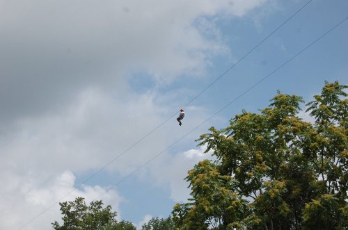 A person zip-lining above trees against a backdrop of cloudy skies.