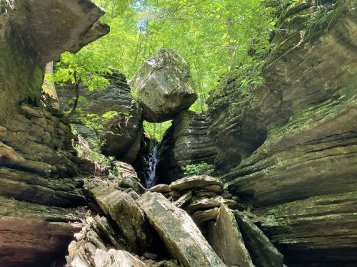 A rocky landscape with large boulders and a small waterfall, surrounded by lush green trees.