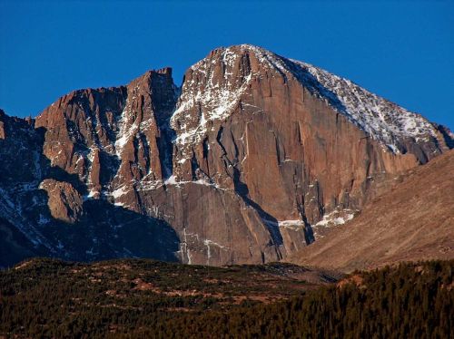 A majestic mountain peak with rocky cliffs and a dusting of snow against a clear blue sky.