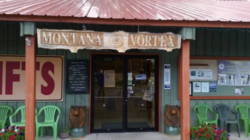 Entrance to Montana Vortex, featuring a wooden sign and colorful flower pots outside.