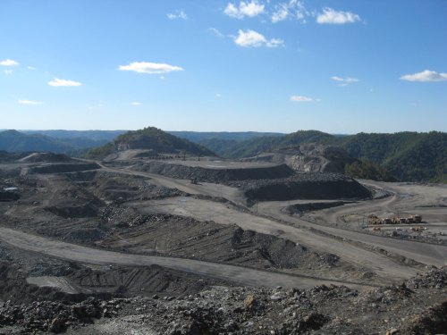 A vast, open mining site with rocky terrain and distant hills under a clear blue sky.