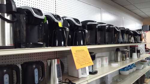 A row of various coffee makers and kettles displayed on a shelf in a store.