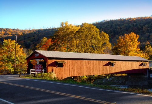 A red covered bridge surrounded by vibrant autumn trees and a clear blue sky.