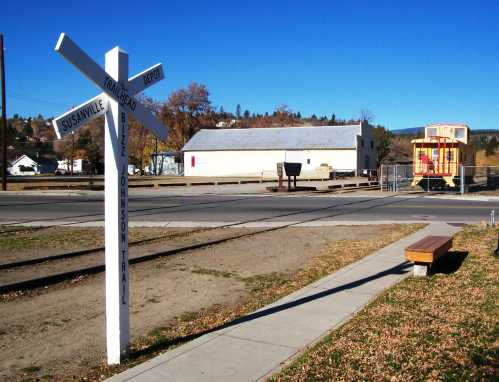 Signpost at a train crossing with directions to Susanville and Johnson Trail, featuring a playground in the background.